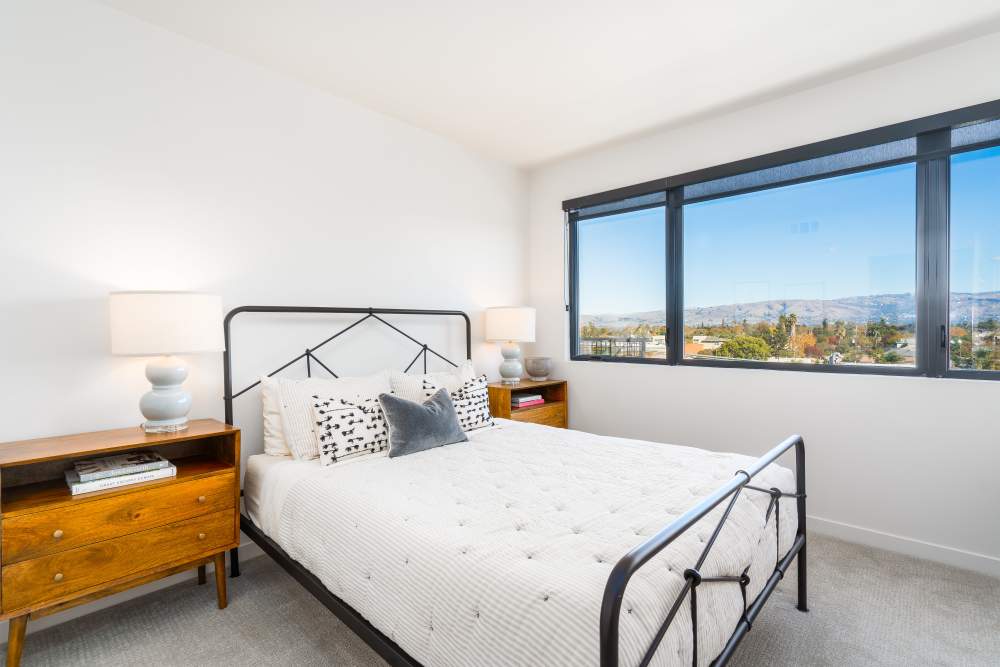 Bright bedroom with large windows, cozy bed, and stylish wooden nightstands at Exhibit at J Town in San Jose, California