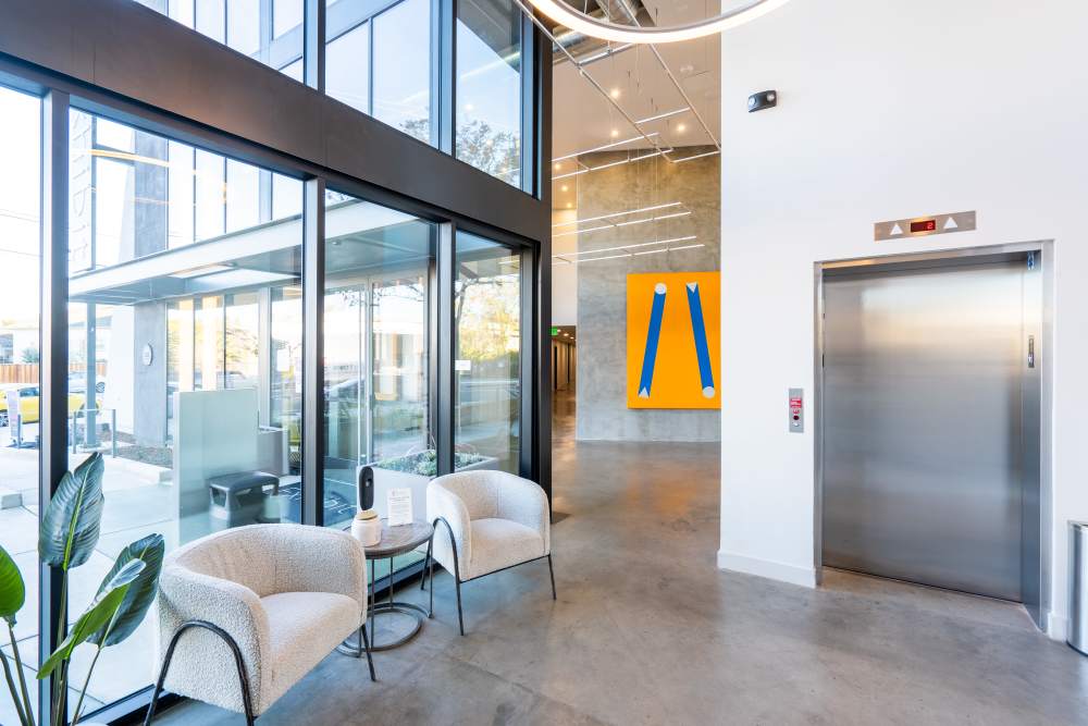 Bright lobby with large windows, modern seating, and an elevator, featuring contemporary artwork on the wall at Exhibit at J Town in San Jose, California
