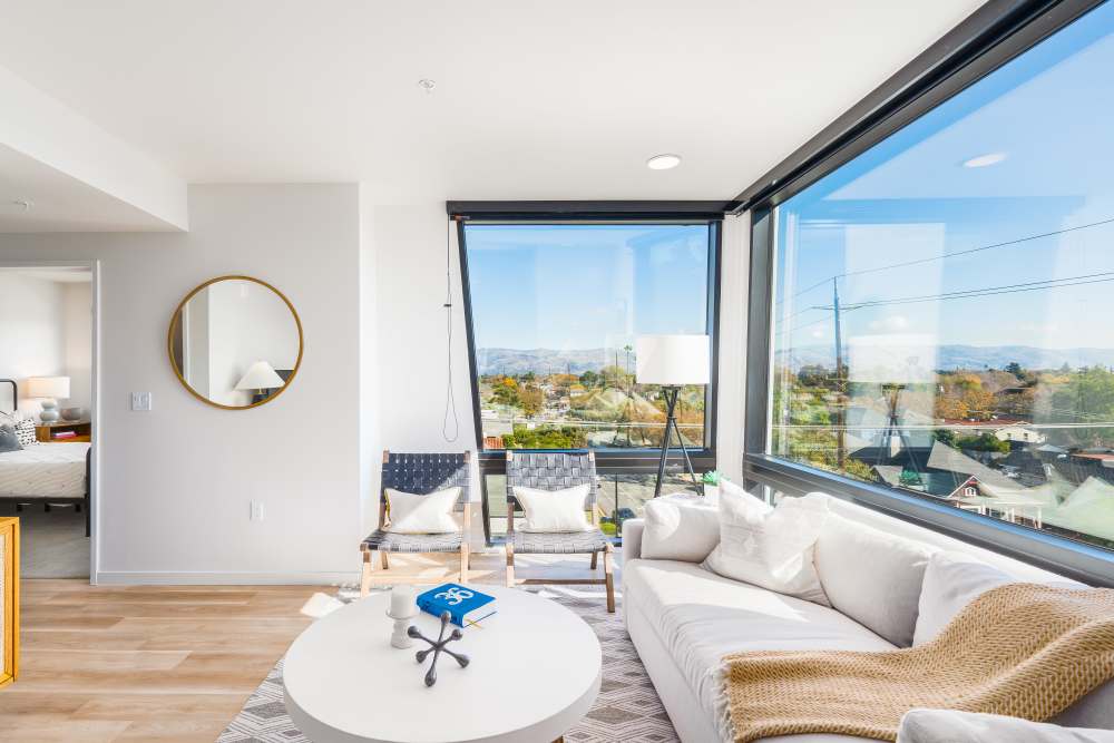 Bright living room with large windows, wood-style flooring, modern furnishings, and scenic views at Exhibit at J Town in San Jose, California
