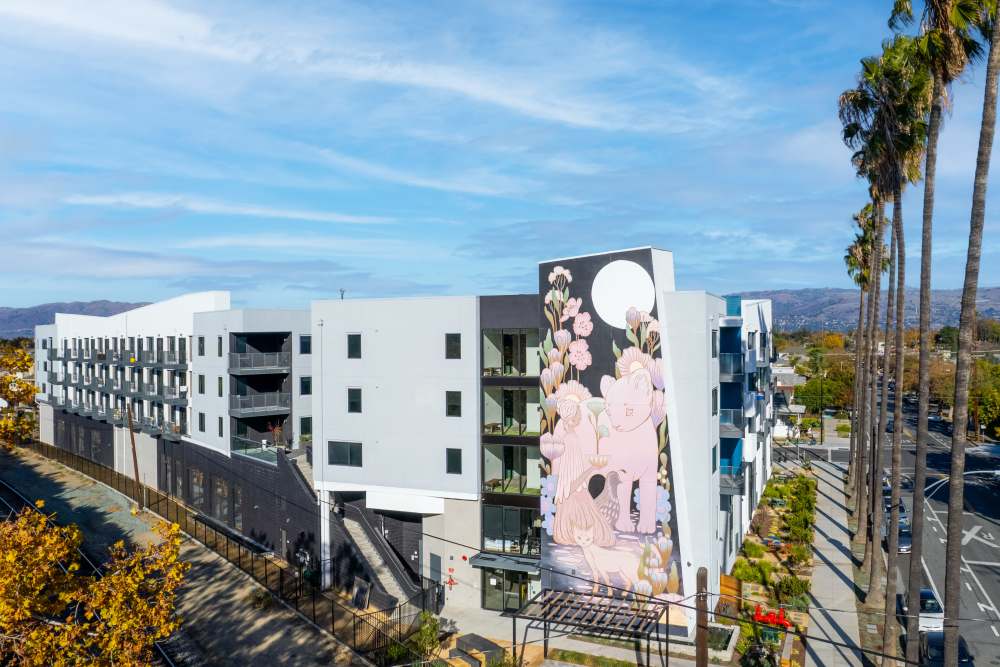Modern apartment community with vibrant mural and palm trees along the street at Exhibit at J Town in San Jose, California