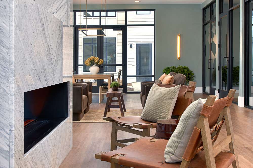 Fireplace lounge with leather chairs, wood beams, and floor‑to‑ceiling windows at The Millwright in Cornelius, North Carolina