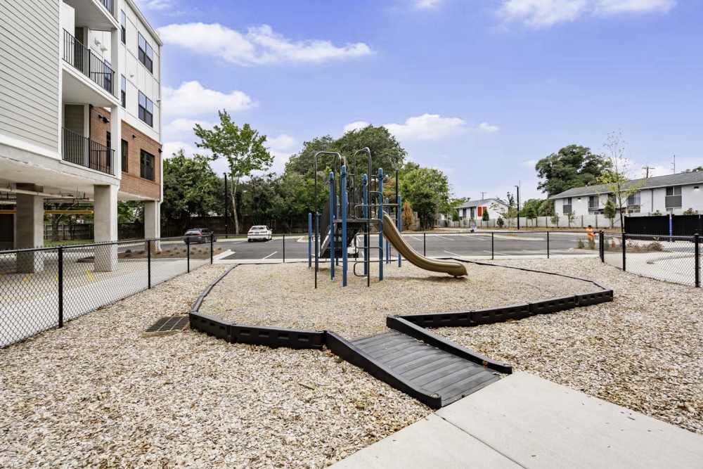 Playground area with slide and swings, surrounded by a fenced gravel surface and greenery at Benton Crossing I in Columbia, South Carolina