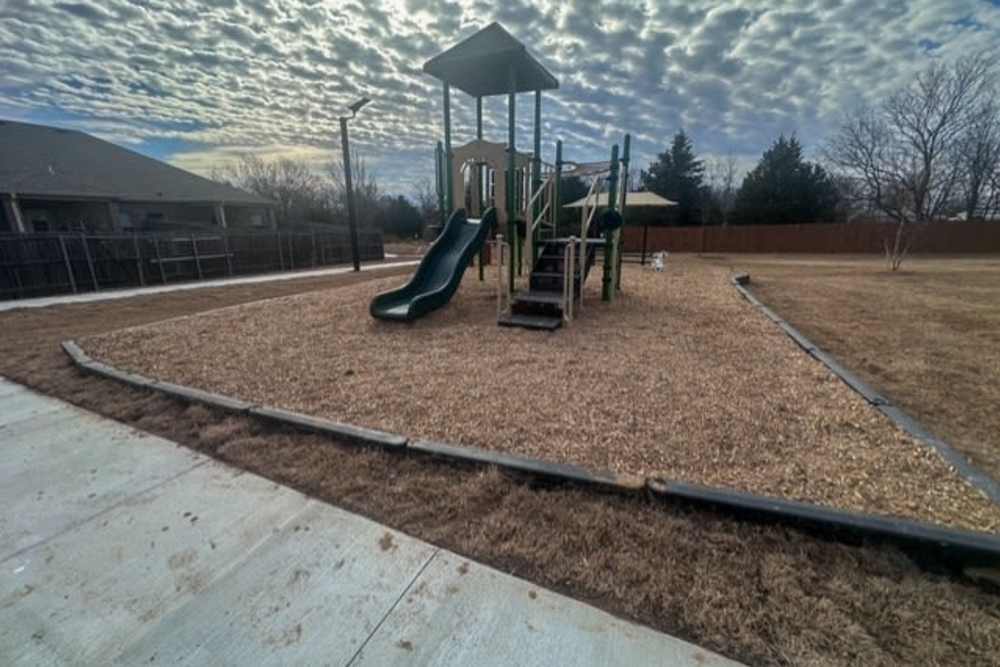 Playground with slide in grassy area at Copper Trail Townhomes in Owasso, Oklahoma