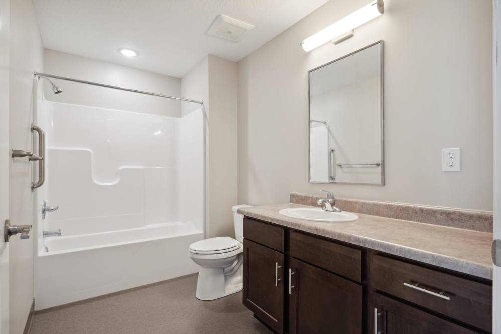 Modern bathroom with a tub-shower combo, dark wood cabinetry, and a large mirror at Chandler Pointe in Wilton, Iowa
