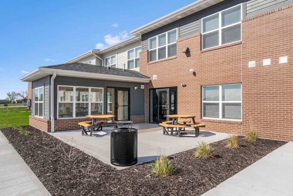 Outdoor seating area with picnic tables and landscaped surroundings near apartment entrance at Chandler Pointe in Wilton, Iowa