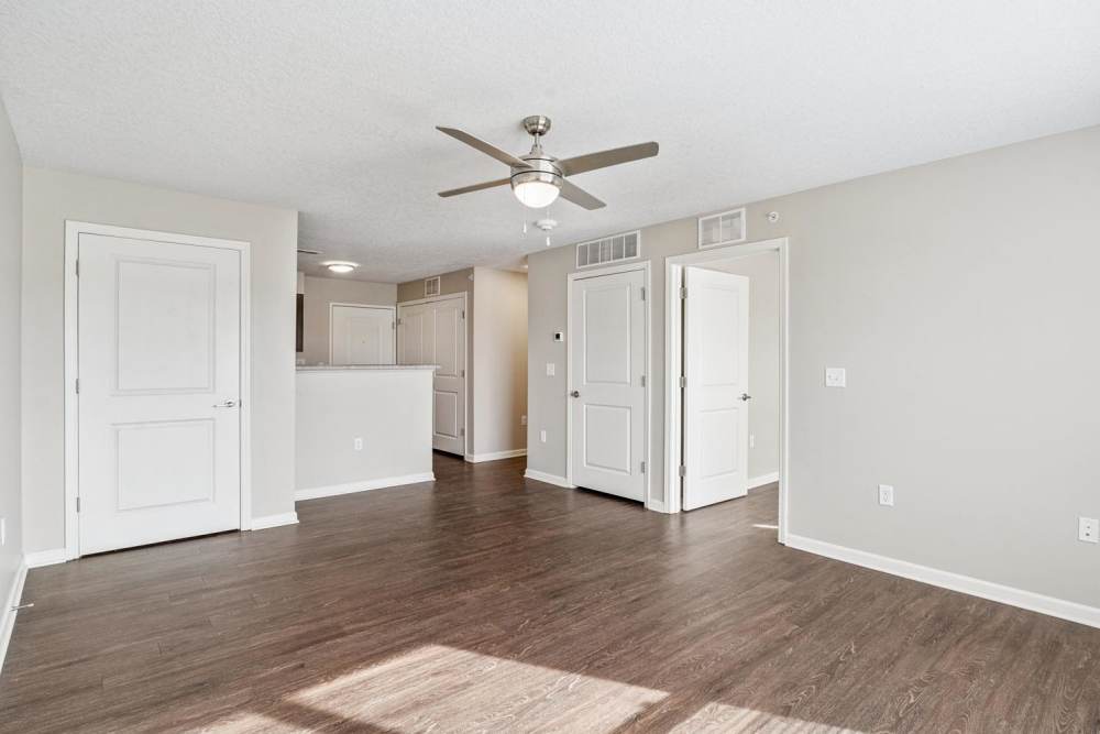 Spacious living area with wood-style flooring and ceiling fan, open layout, natural light streaming in at Johnston Crossing I in Johnston, Iowa