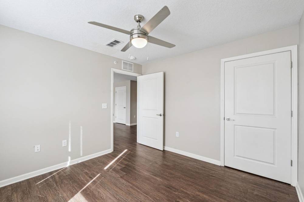 Spacious bedroom with wood-style flooring and ceiling fan, featuring neutral walls and natural light at Johnston Crossing I in Johnston, Iowa