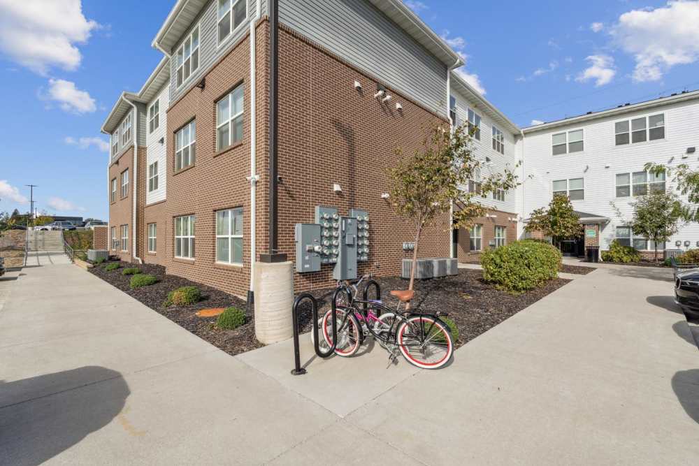 Bicycles parked near a modern apartment building with landscaped greenery and walkways at Johnston Crossing I in Johnston, Iowa