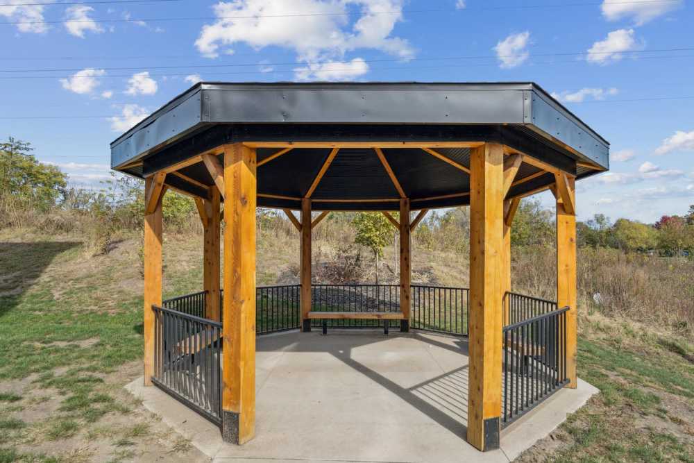 Wooden gazebo with black roof and seating area surrounded by grassy landscape and trees at Johnston Crossing I in Johnston, Iowa