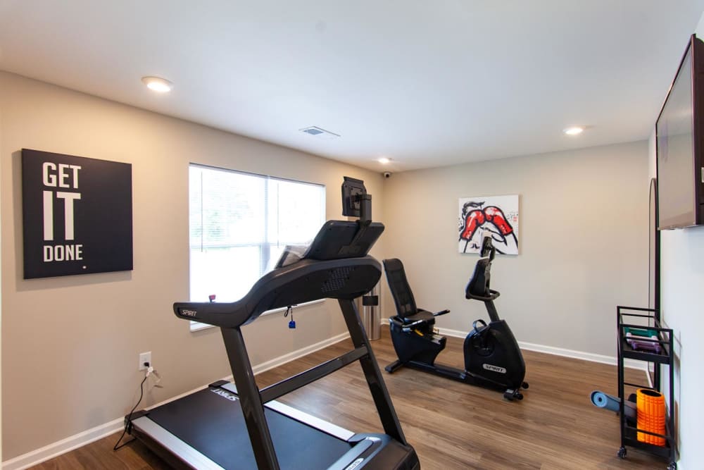 Fitness room with treadmill, stationary bike, wood-style flooring, motivational wall art, and natural light from windows at Palatine Meadows in New Bern, North Carolina
