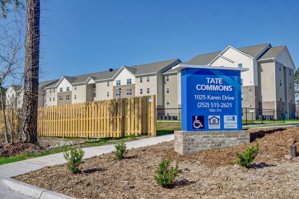 Gated entrance with wooden fence and landscaped area in front of apartment buildings at Tate Commons in New Bern, North Carolina