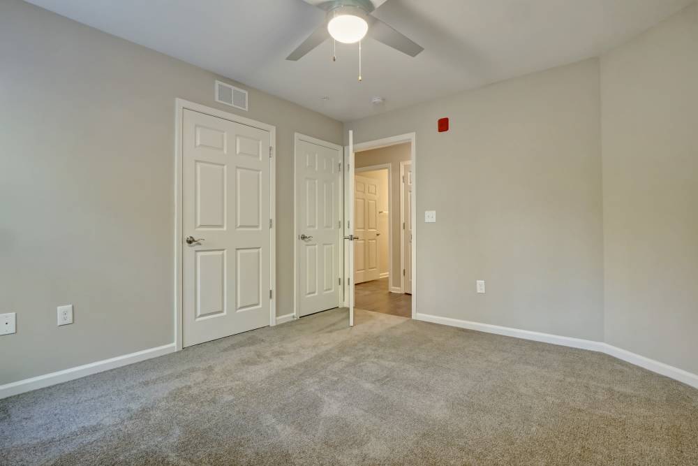 Spacious bedroom with carpet flooring and ceiling fan, featuring two closed doors and neutral walls at Tate Commons in New Bern, North Carolina