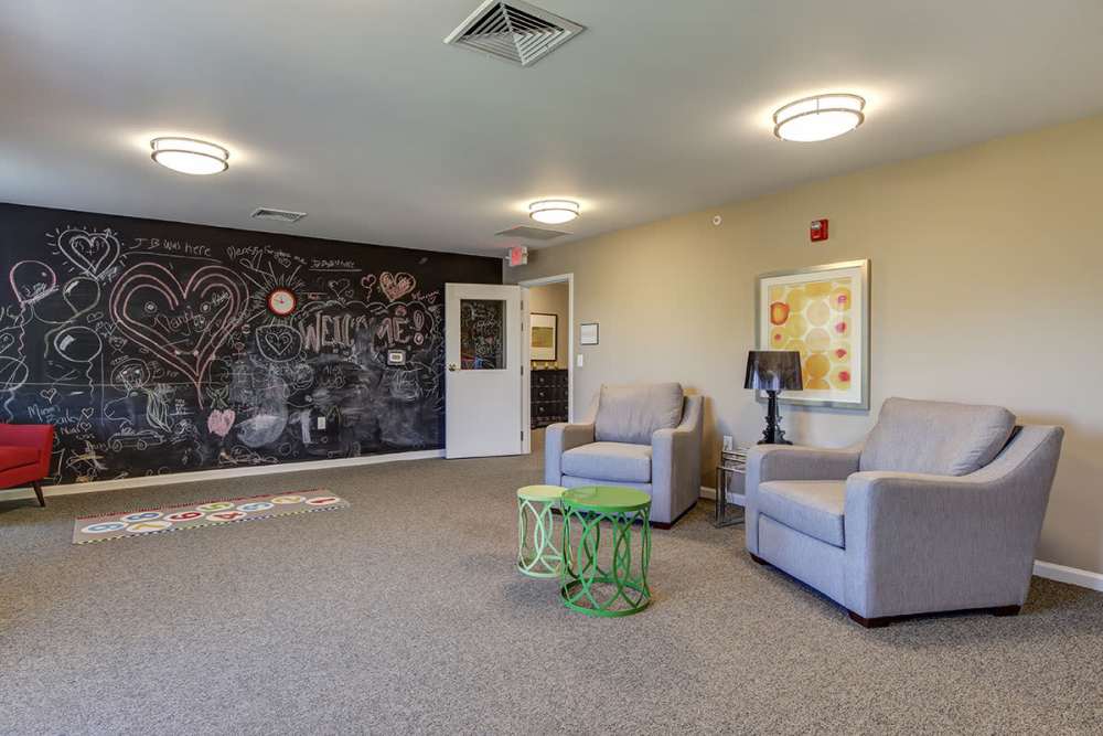 Cozy lounge area with chalkboard wall, two armchairs, green accent table, and colorful rug at Viewmont Square in Hickory, North Carolina