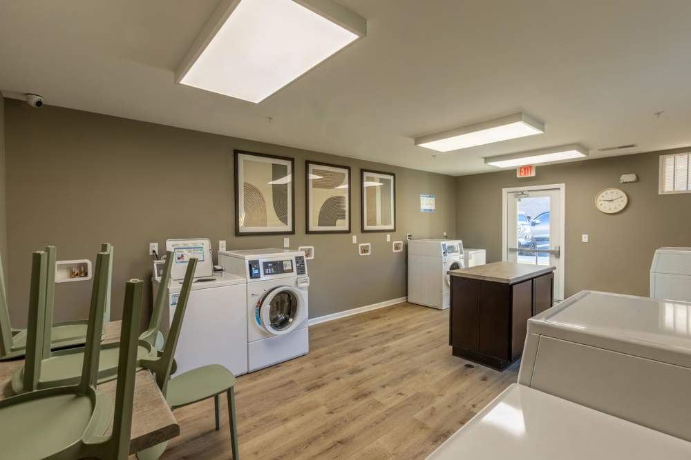 Bright laundry room with modern machines, wood-style flooring, and seating area for convenience at Clemons Greene in Lexington, South Carolina