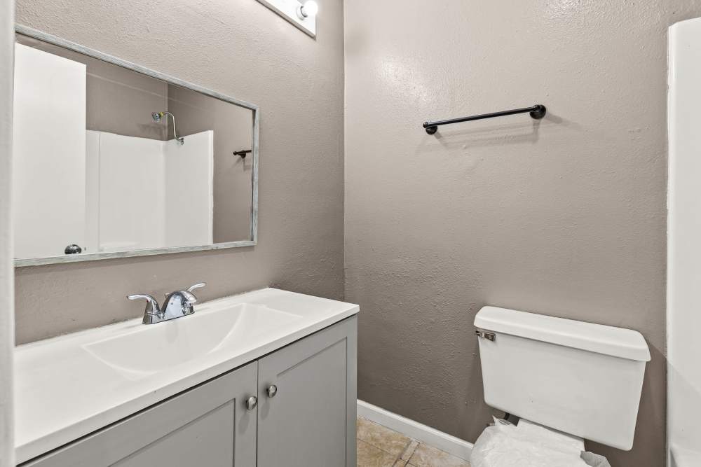 Modern bathroom with gray cabinetry, large mirror, and shower area with white tiles at Towne East Village Apartment Homes in Converse, Texas