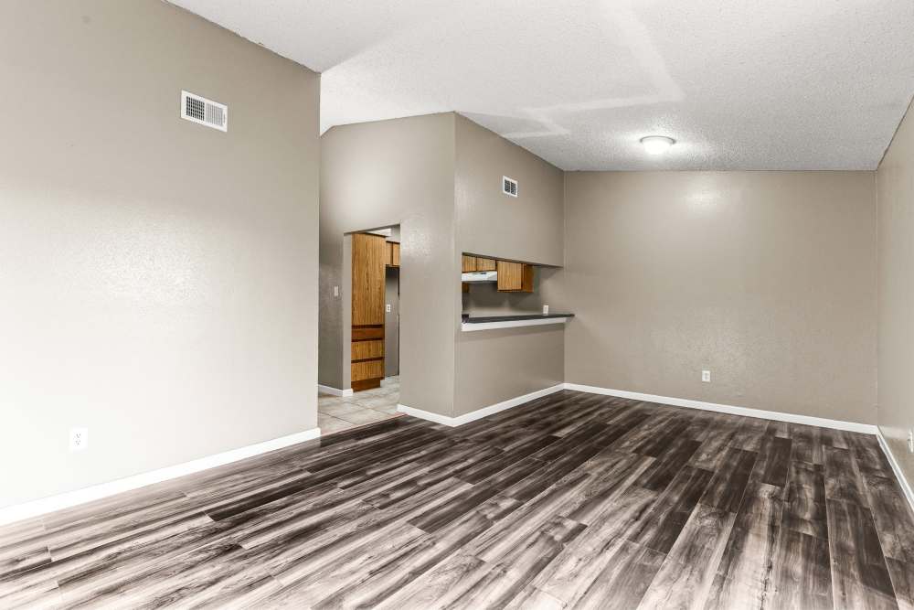 Spacious living area with wood-style flooring and open layout leading to kitchen at Towne East Village Apartment Homes in Converse, Texas