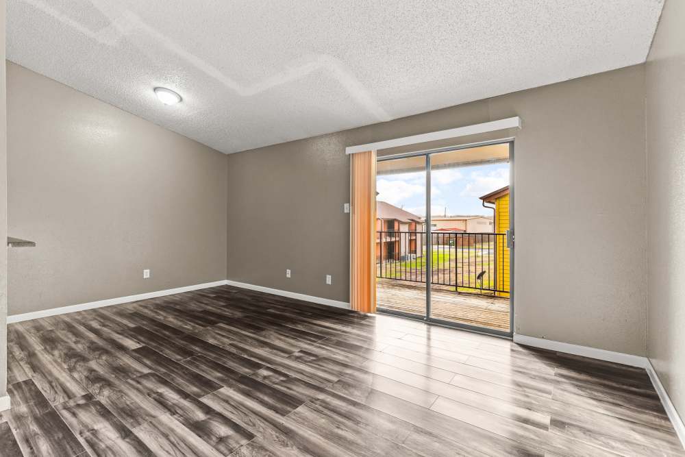 Spacious living area with wood-style flooring and sliding glass door to private balcony at Towne East Village Apartment Homes in Converse, Texas