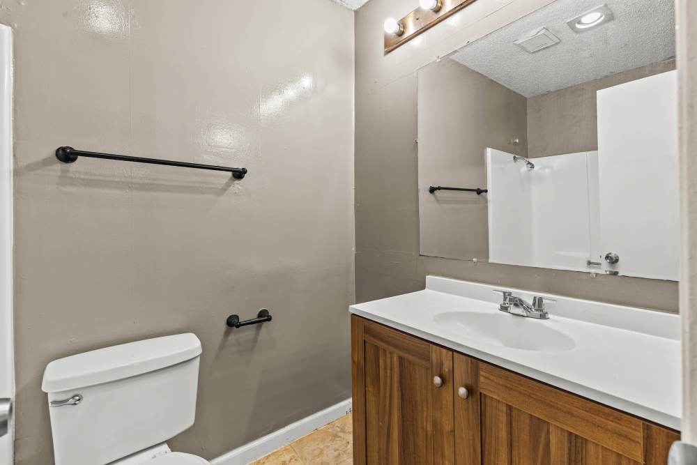 Modern bathroom with wood cabinetry, white countertop, and large mirror, featuring grab bars for accessibility at Towne East Village Apartment Homes in Converse, Texas