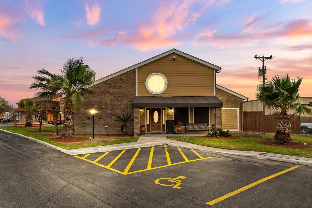Gated entrance with palm trees and sunset sky, accessible parking in front of apartment community at Towne East Village Apartment Homes in Converse, Texas