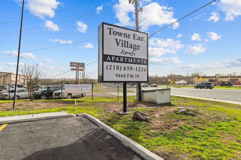 Sign for Towne East Village Apartments with clear blue sky and grassy area at Towne East Village Apartment Homes in Converse, Texas
