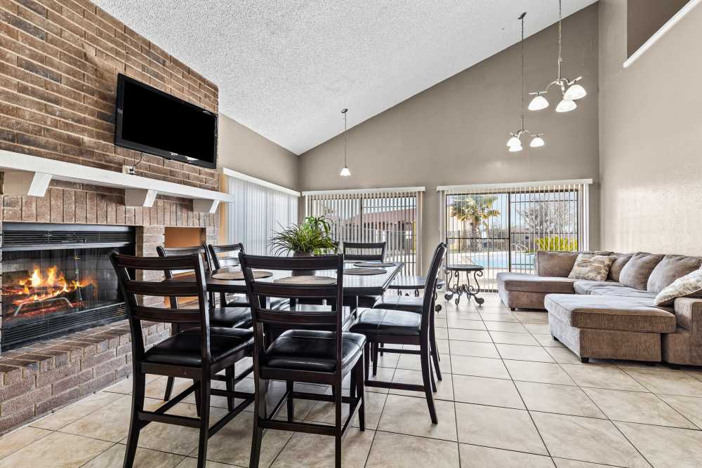 Bright community lounge with dining table, fireplace, and large windows overlooking the pool area at Towne East Village Apartment Homes in Converse, Texas