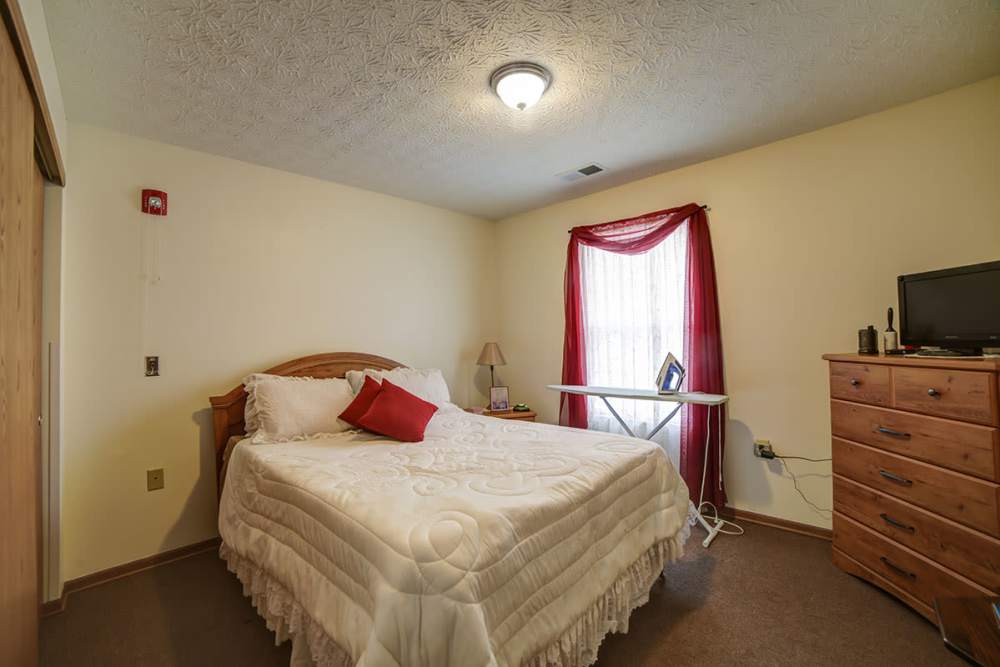 Cozy bedroom with a queen bed, dresser, and window with red curtains at Madison Grove in Slippery Rock, Pennsylvania
