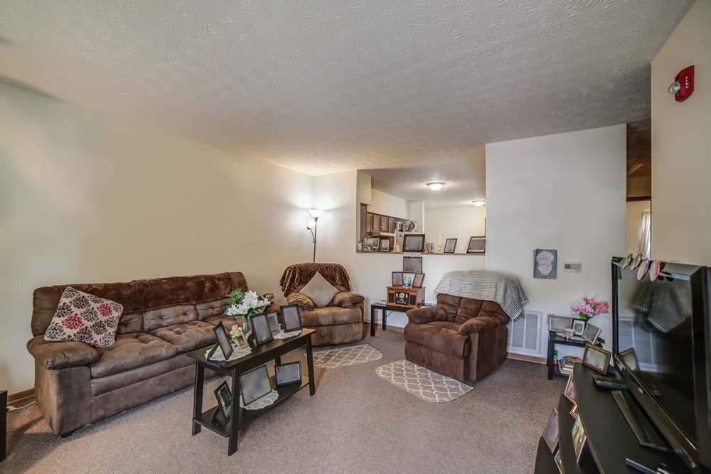 Cozy living room with brown sofas, decorative pillows, and a coffee table with framed photos at Madison Grove in Slippery Rock, Pennsylvania