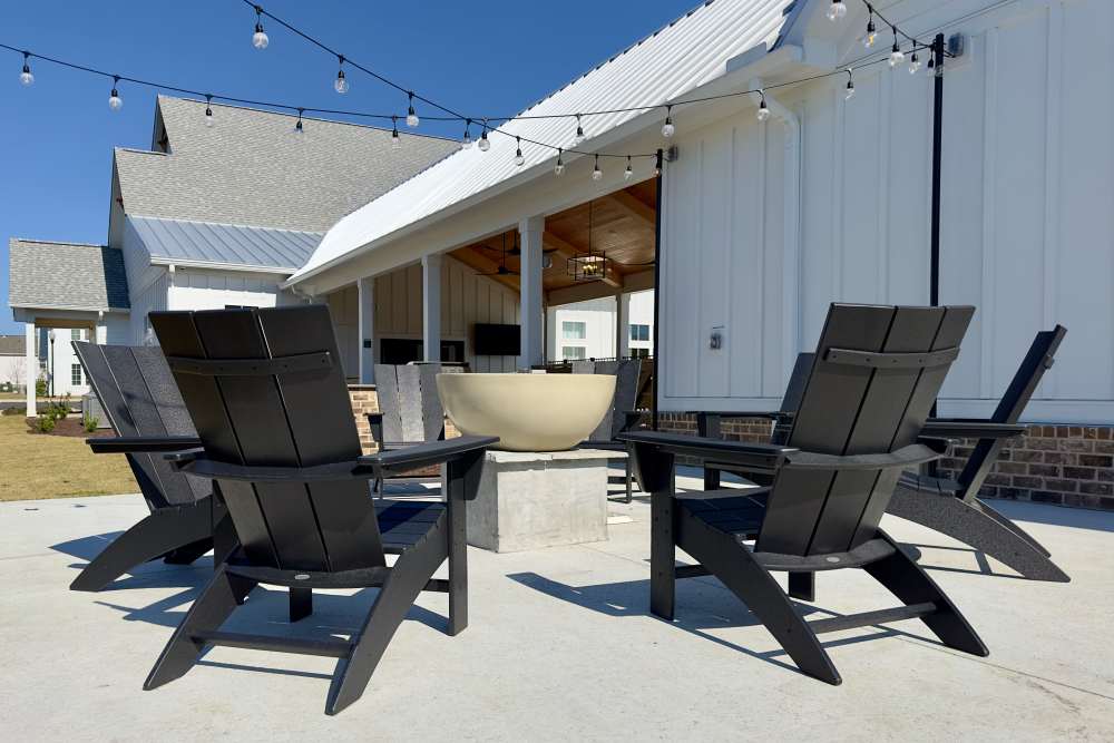 Outdoor seating area with black Adirondack chairs around a fire pit and string lights overhead at Encore at Westgate in Leland, North Carolina