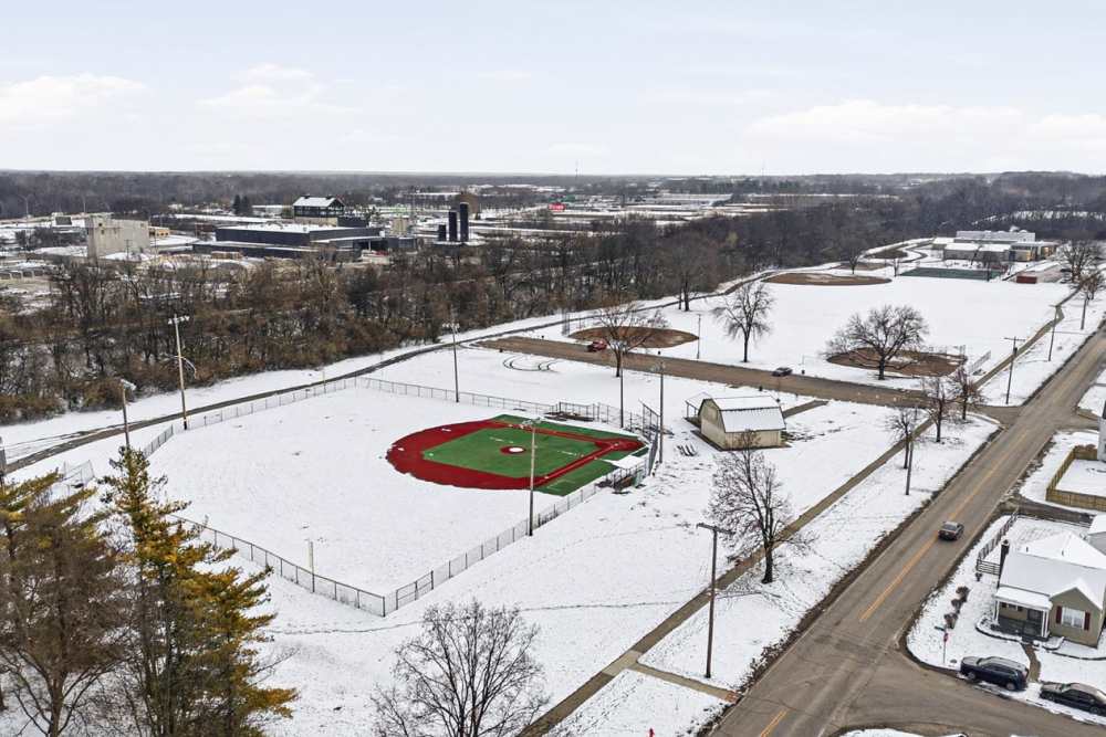 Snow-covered baseball field with surrounding trees and nearby road at Granville Woods Lofts in Columbus, Ohio