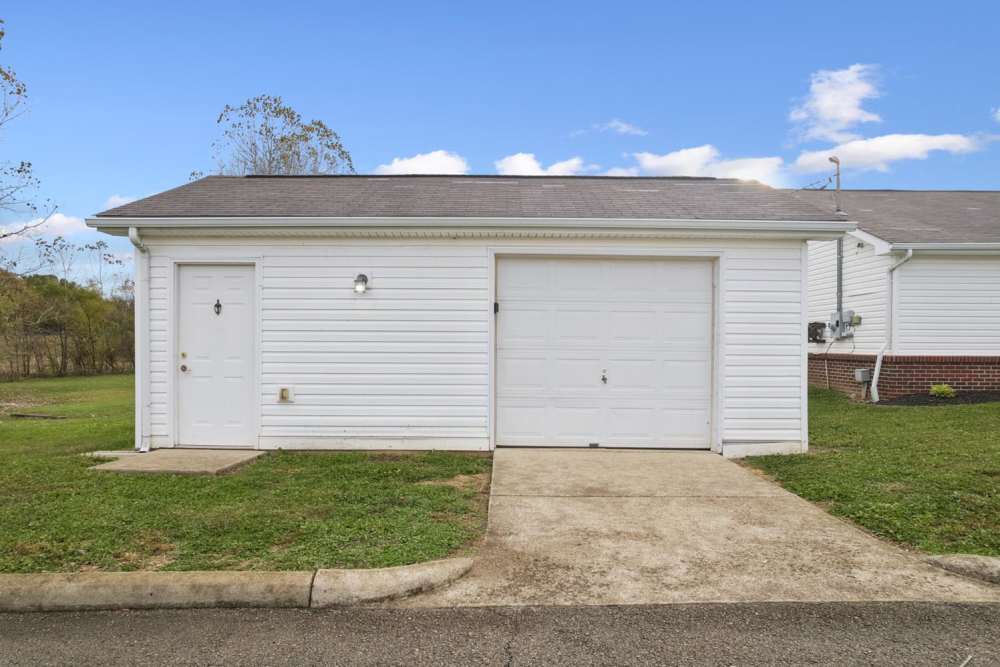 Single-story white apartment with a garage and grassy area at Webster Glen in Peebles, Ohio