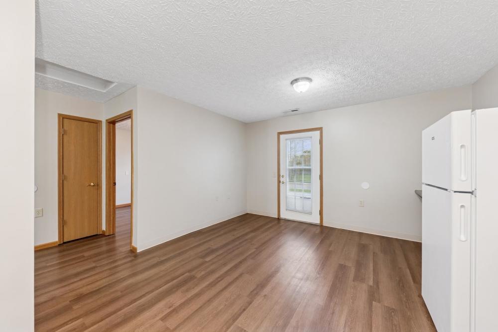 Open layout living space with wood-style flooring and a white refrigerator at Webster Glen in Peebles, Ohio