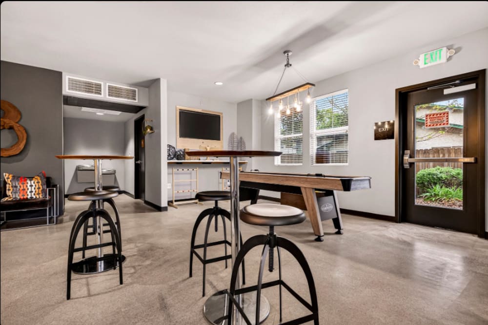 Game room: Community lounge with bar stools, high tables, pool table, wall-mounted TV, and exit door at Cedar Flats in Chico, California  