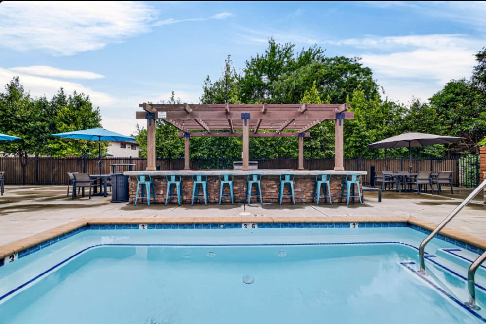 Pool area: Outdoor pool with pergola-covered bar seating, high stools, umbrellas, and surrounding trees at Cedar Flats in Chico, California  