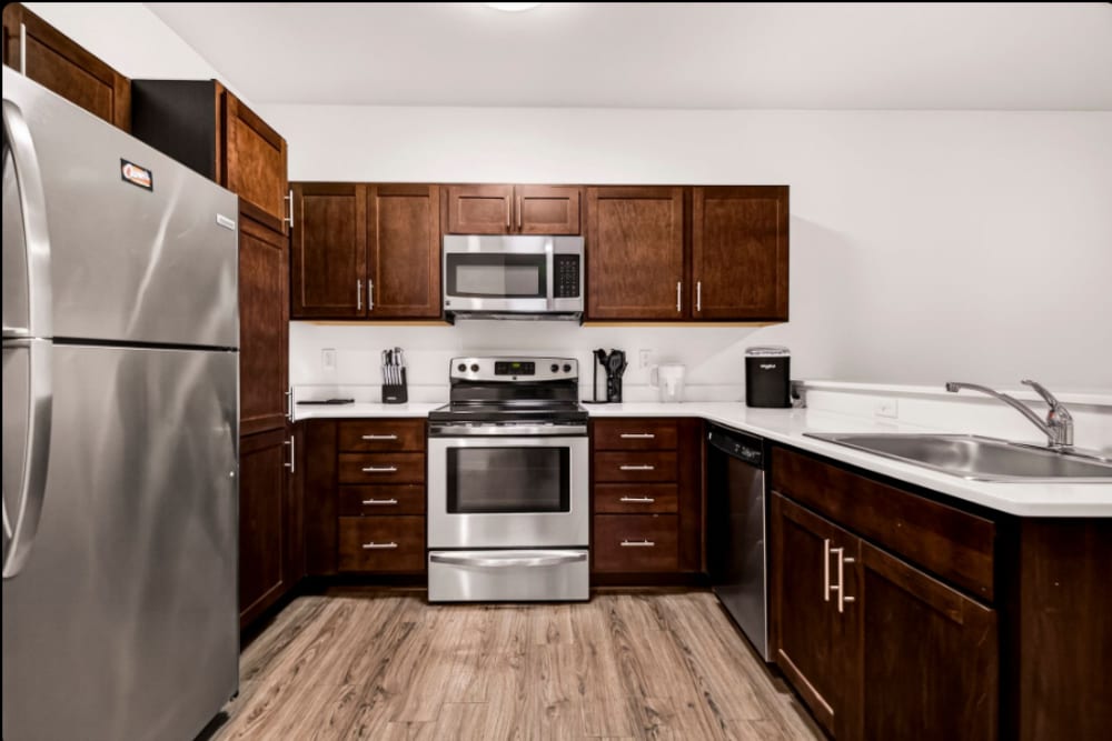 Kitchen: U-shaped kitchen with stainless steel appliances, dark cabinets, sink, and wood-style flooring at Cedar Flats in Chico, California  