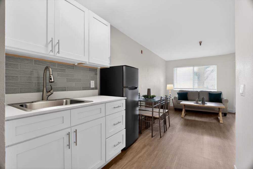 Compact kitchen with white cabinets, sink, black refrigerator, and dining area beyond at Whealdon Estates by Barclay House in Baton Rouge, Louisiana  