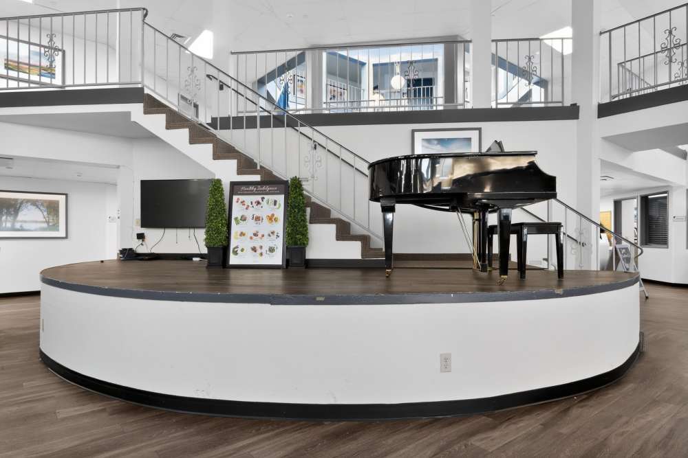 Lobby with raised circular stage, grand piano, staircase, and open second-floor railing at Whealdon Estates by Barclay House in Baton Rouge, Louisiana  