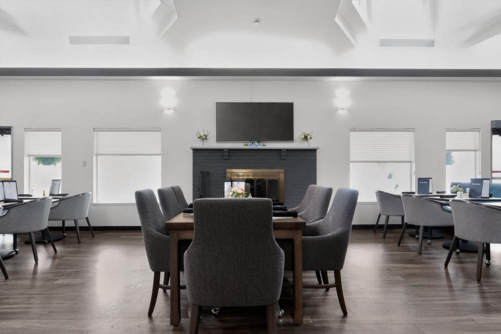 Dining room with long table, fireplace, wall-mounted TV, and windows on both sides at Whealdon Estates by Barclay House in Baton Rouge, Louisiana  