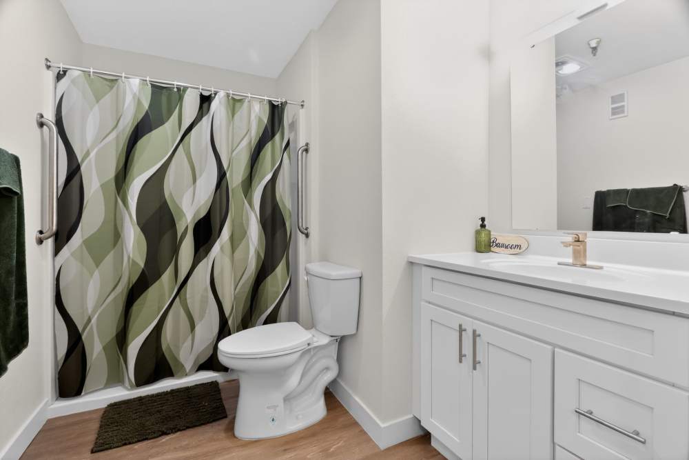 Bathroom with vanity, mirror, toilet, and shower with green patterned curtain at Whealdon Estates by Barclay House in Baton Rouge, Louisiana  