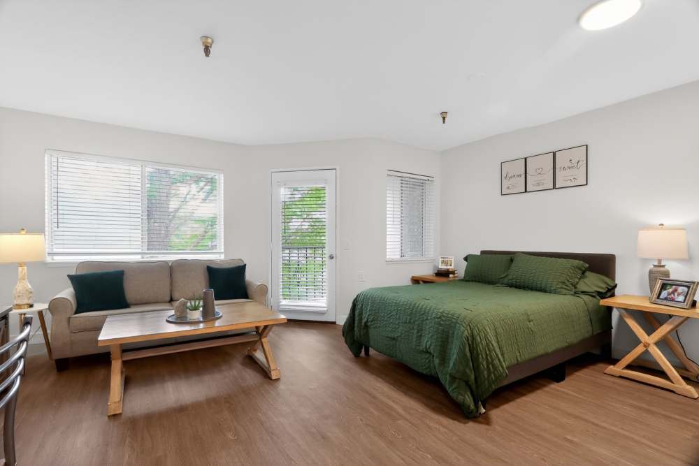 Bedroom with bed, green bedding, sofa, coffee table, side tables, and windows at Whealdon Estates by Barclay House in Baton Rouge, Louisiana  