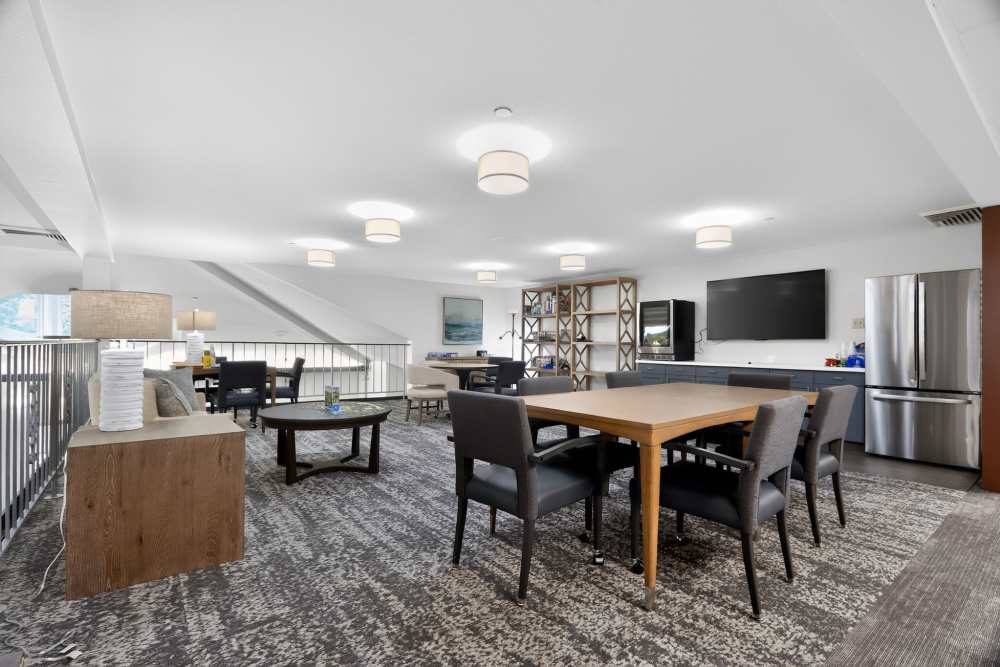 Common area with tables, TV, shelving, kitchenette, and soft overhead lighting at Whealdon Estates by Barclay House in Baton Rouge, Louisiana  