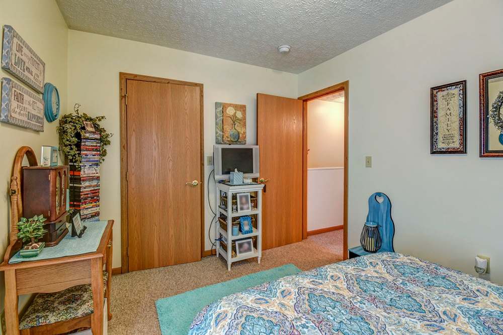 Cozy bedroom with carpeted flooring, wooden furniture, and decorative wall art at Canterbury Place in Elkins, West Virginia