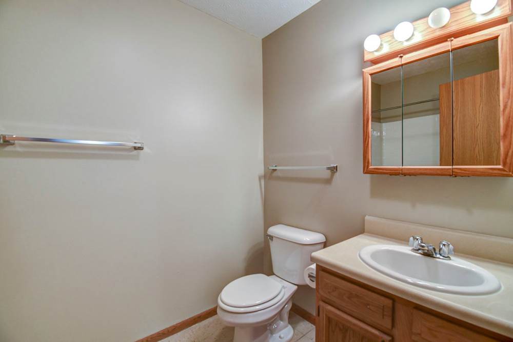 Bright bathroom with beige walls, wooden cabinetry, and a large mirror above the sink at Oakmont Greene II in Mount Hope, West Virginia