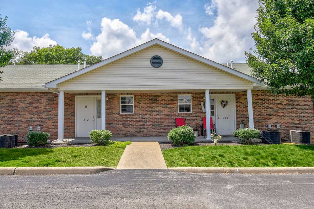 Two apartment entrances with brick exteriors, green lawns, and small shrubs, sunny day with clouds at Oakmont Greene II in Mount Hope, West Virginia