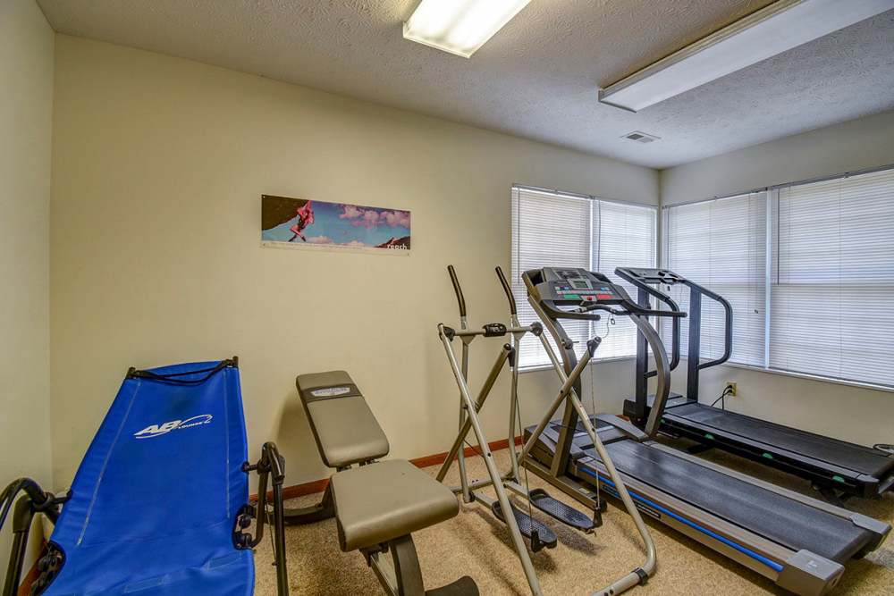 Fitness room with treadmill, elliptical, and weight bench near large windows at Oakmont Greene II in Mount Hope, West Virginia