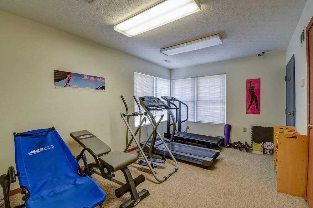 Bright fitness room with treadmill, exercise bike, and blue lounge chair against light walls at Oakmont Greene II in Mount Hope, West Virginia