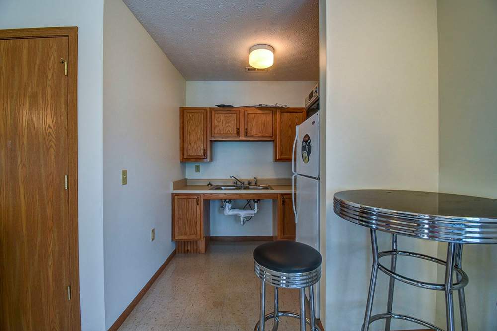 Clubhouse kitchen with wooden cabinets, stainless steel appliances, and a bar table with stools at Oakmont Greene II in Mount Hope, West Virginia