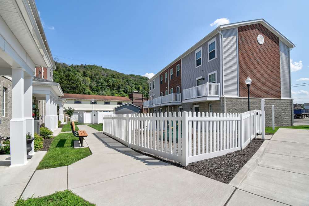 Gated entrance with white fencing, landscaped pathways, and benches near apartment buildings at Labelle Greene I in Wheeling, West Virginia