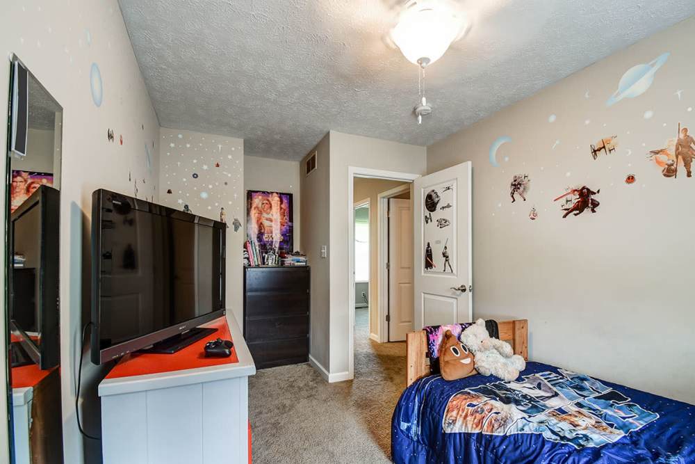 Cozy bedroom with carpeted flooring, TV, and themed wall decals, featuring a bed with colorful bedding at Terrapin Park in Parkersburg, West Virginia