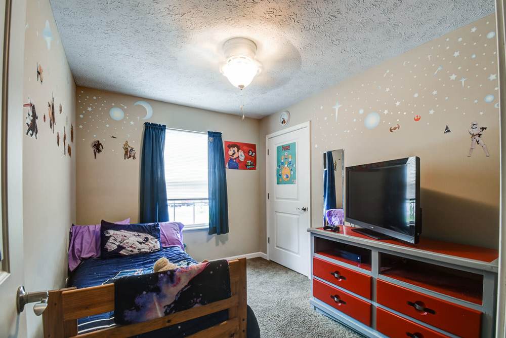 Cozy bedroom with space-themed decor, blue curtains, and a TV on a red dresser at Terrapin Park in Parkersburg, West Virginia