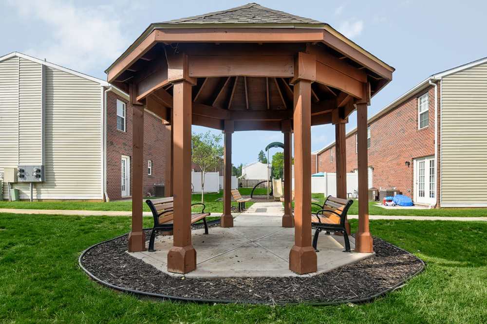 Wooden gazebo with seating surrounded by green grass and apartment buildings in the background at Terrapin Park in Parkersburg, West Virginia